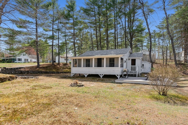 view of front of house with roof with shingles, a wooden deck, a sunroom, and a front lawn