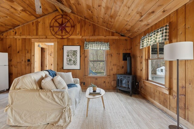living room with wooden walls, lofted ceiling with beams, wood finished floors, and a wood stove