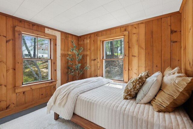 bedroom with wooden walls, multiple windows, and carpet