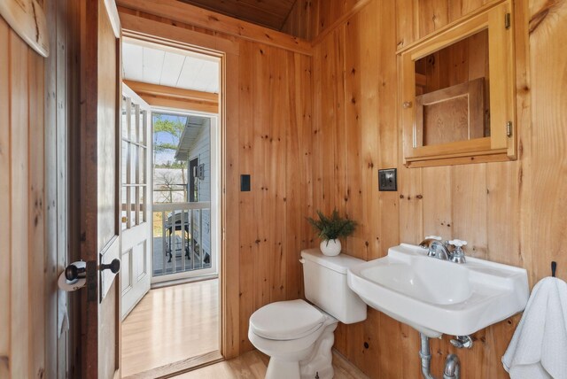 bathroom with wooden walls, toilet, and a sink