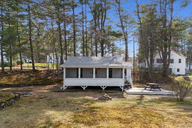 exterior space with a fire pit, a wooden deck, roof with shingles, a sunroom, and a lawn