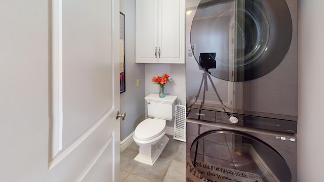 bathroom with toilet, baseboards, stacked washer / dryer, and tile patterned floors