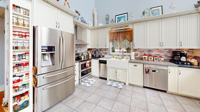 kitchen with light tile patterned flooring, a sink, appliances with stainless steel finishes, backsplash, and wall chimney exhaust hood