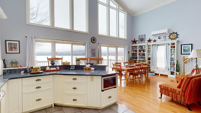 kitchen featuring ornamental molding, dark stone countertops, built in microwave, an AC wall unit, and light wood-style floors