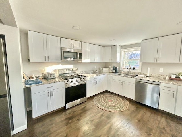 kitchen with appliances with stainless steel finishes, dark wood-style flooring, white cabinetry, and a sink