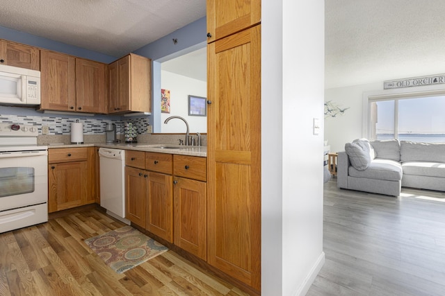 kitchen with light wood finished floors, tasteful backsplash, light countertops, a sink, and white appliances