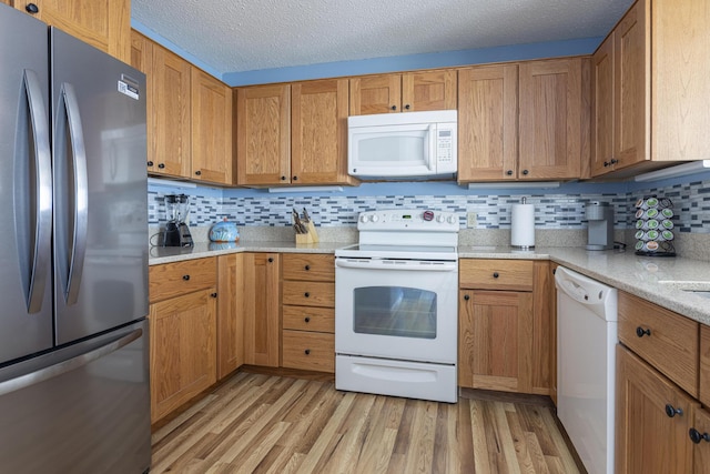 kitchen featuring backsplash, brown cabinetry, a textured ceiling, light wood-type flooring, and white appliances