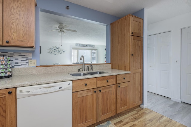 kitchen featuring light countertops, backsplash, light wood-style floors, white dishwasher, and a sink