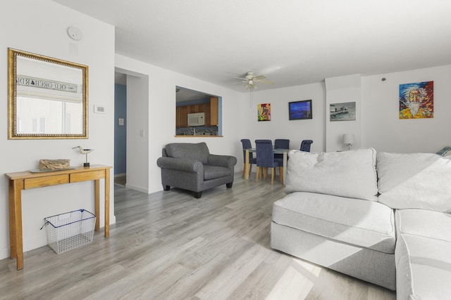 living room featuring light wood-style floors, baseboards, and a ceiling fan