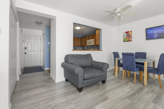 dining space featuring a textured ceiling, a ceiling fan, light wood-style flooring, and baseboards