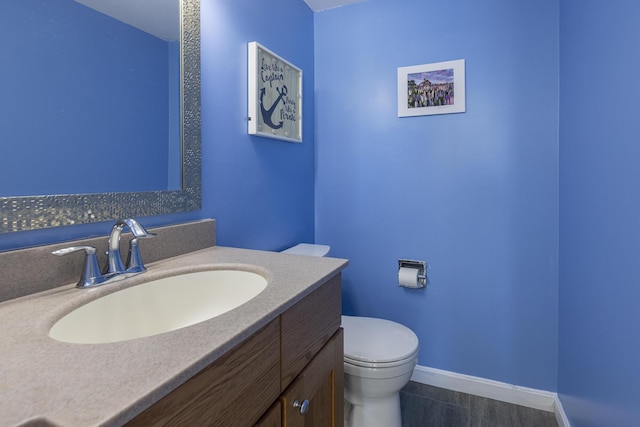 half bathroom featuring baseboards, vanity, and toilet