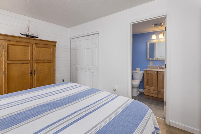 bedroom featuring a textured ceiling, connected bathroom, dark wood-style flooring, visible vents, and a closet