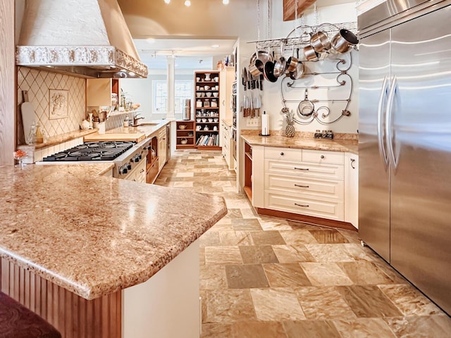 kitchen with stove, stone finish flooring, ventilation hood, a sink, and built in fridge