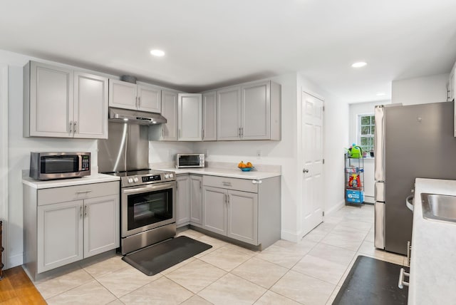 kitchen featuring light tile patterned floors, gray cabinetry, stainless steel appliances, light countertops, and under cabinet range hood