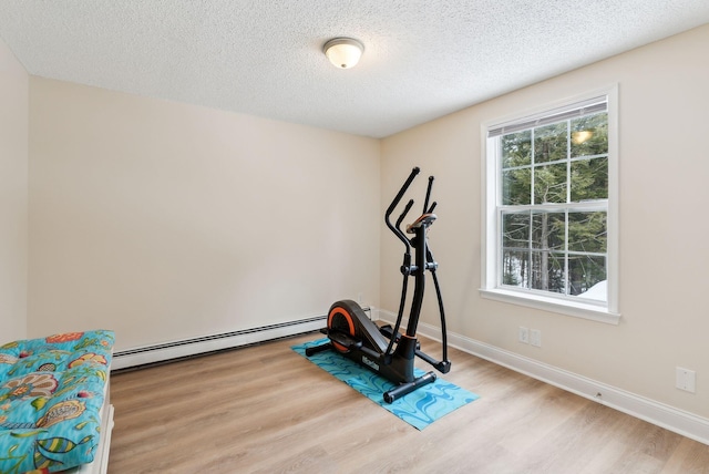 workout room featuring wood finished floors, baseboards, baseboard heating, and a textured ceiling