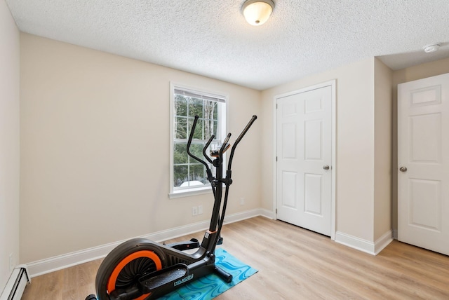 exercise area featuring baseboards, baseboard heating, light wood-style flooring, and a textured ceiling