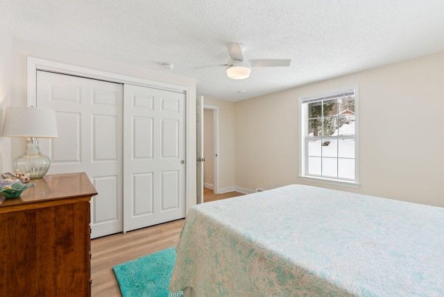 bedroom with baseboards, light wood-style floors, a closet, a textured ceiling, and a ceiling fan