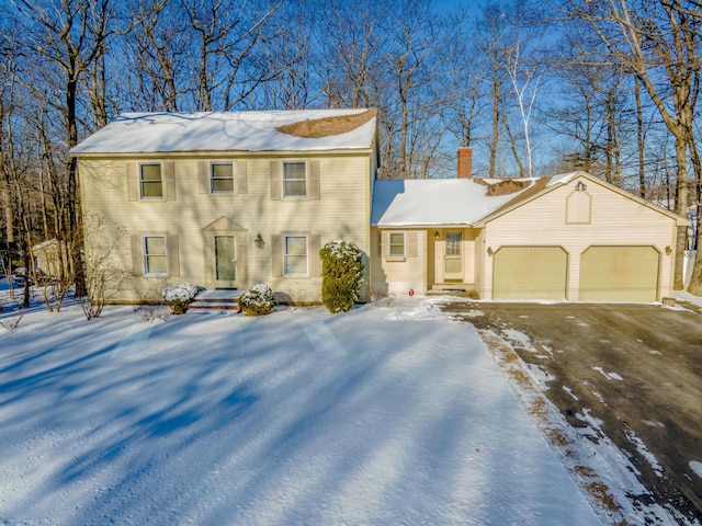 colonial inspired home featuring a garage, driveway, and a chimney