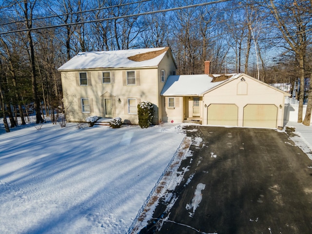 colonial home featuring aphalt driveway, a chimney, and an attached garage