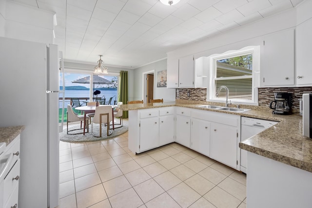 kitchen with a peninsula, white appliances, a sink, decorative backsplash, and plenty of natural light