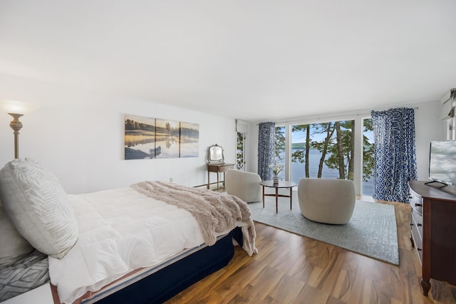 bedroom featuring expansive windows, a baseboard heating unit, and wood finished floors