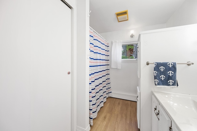 full bathroom featuring curtained shower, a baseboard heating unit, wood finished floors, vanity, and visible vents