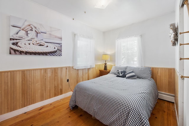 bedroom with hardwood / wood-style flooring, baseboard heating, and wainscoting