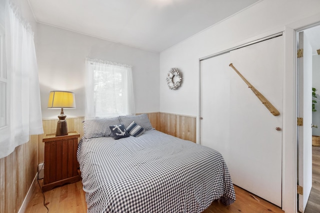 bedroom featuring a closet, a wainscoted wall, wood walls, and wood finished floors