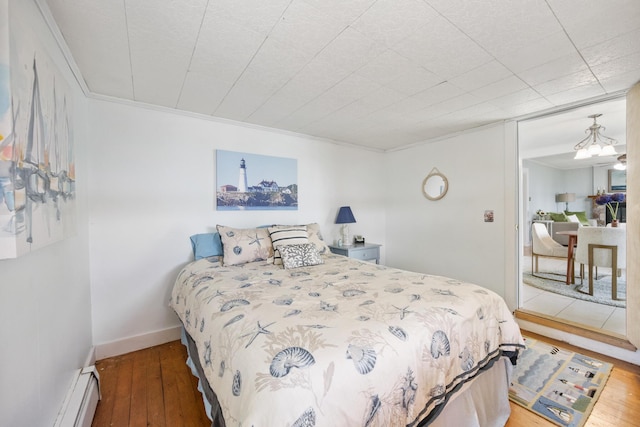 bedroom featuring a baseboard heating unit, crown molding, baseboards, and hardwood / wood-style flooring