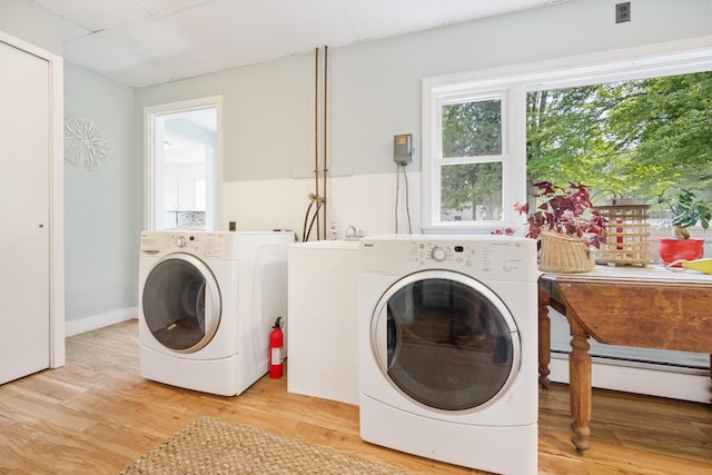 clothes washing area featuring laundry area, light wood-style flooring, a baseboard heating unit, and washer and clothes dryer