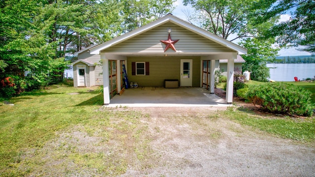 back of property with driveway, a water view, a carport, and a yard