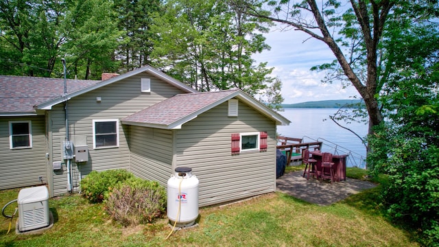 view of home's exterior with roof with shingles, a patio, a chimney, a water view, and a lawn