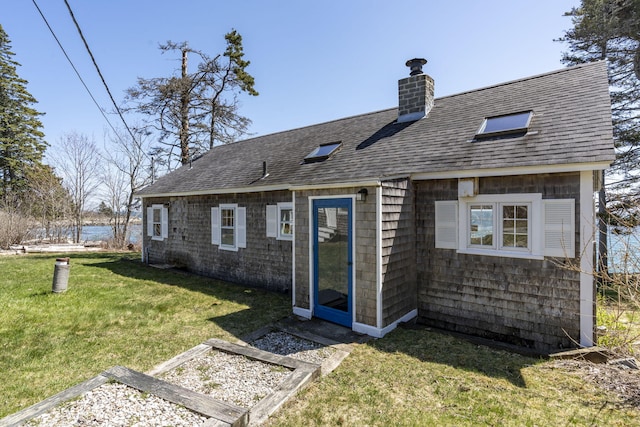 rear view of house with a shingled roof, a water view, a lawn, and a chimney