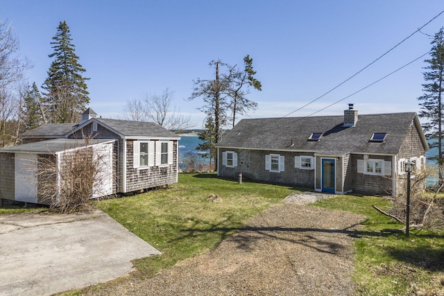 view of front of home with an outbuilding, a detached garage, a chimney, a shingled roof, and a front lawn