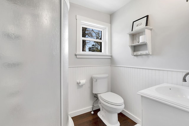 bathroom featuring toilet, wood finished floors, vanity, wainscoting, and a shower stall