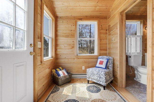 interior space featuring baseboard heating, wooden ceiling, wood finished floors, and wooden walls