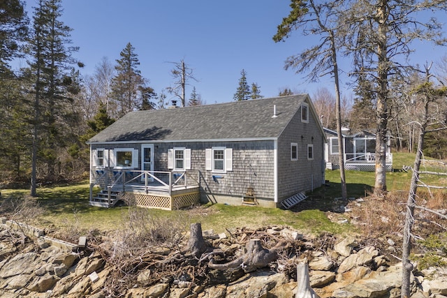 view of front of home with a shingled roof, a front yard, and a wooden deck