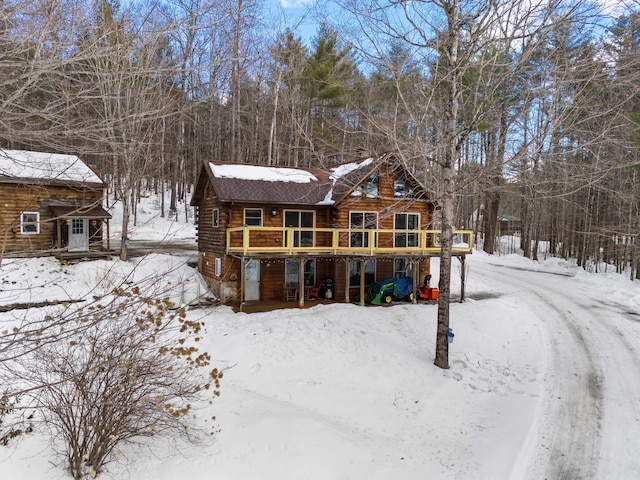 snow covered back of property featuring log exterior and a wooden deck