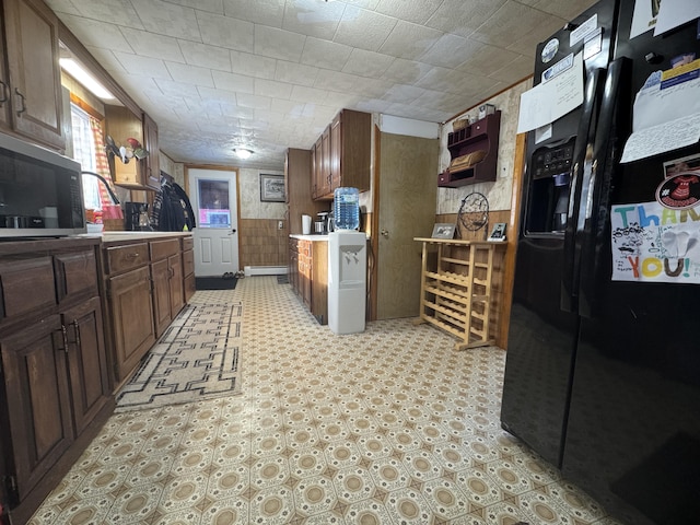 51 N Guilford Rd, Monson, ME 04464 - kitchen with black refrigerator with ice dispenser, stainless steel microwave, light countertops, wooden walls, and light flooring