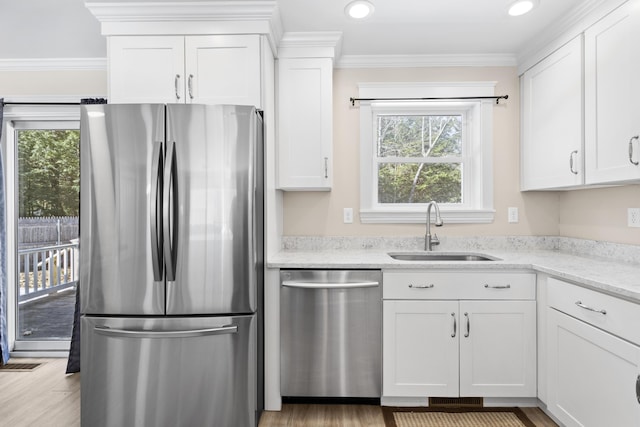 kitchen with light stone counters, ornamental molding, a sink, white cabinets, and appliances with stainless steel finishes