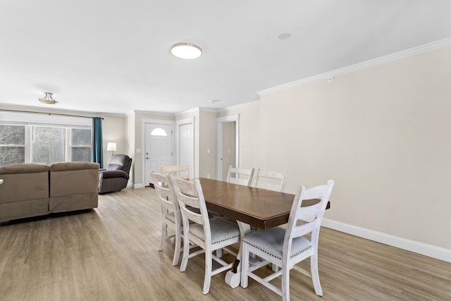 dining room featuring light wood finished floors, crown molding, and baseboards