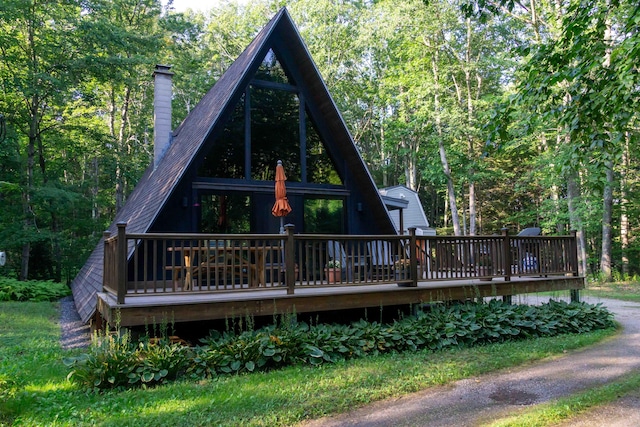 rear view of house with dirt driveway, a chimney, a wooded view, and a wooden deck