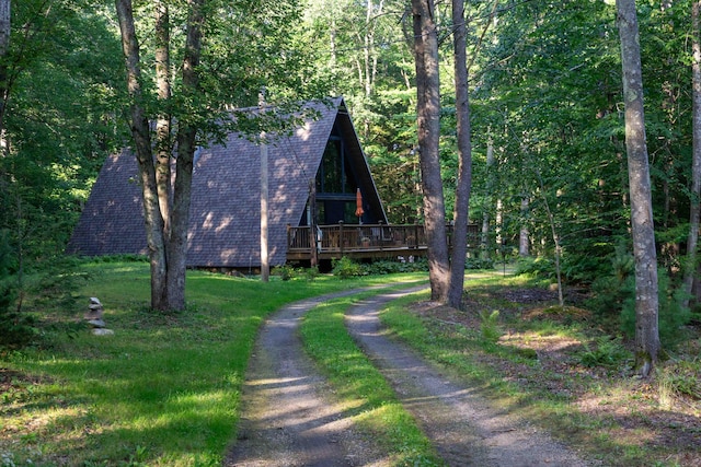 view of front of home with a shingled roof, a forest view, a deck, and dirt driveway