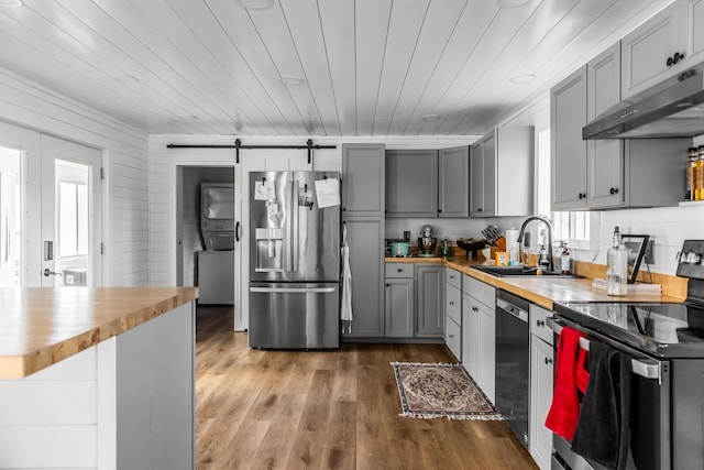 kitchen with stacked washer and clothes dryer, butcher block counters, a barn door, appliances with stainless steel finishes, and under cabinet range hood