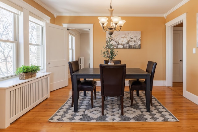 dining area with ornamental molding, light wood finished floors, and an inviting chandelier