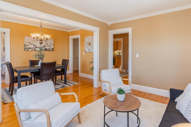 living room with light wood-style flooring, ornamental molding, a chandelier, and baseboards