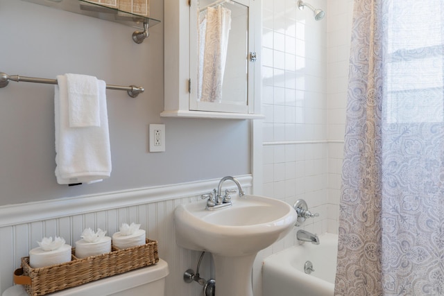 bathroom with wainscoting, a sink, toilet, and shower / tub combo with curtain