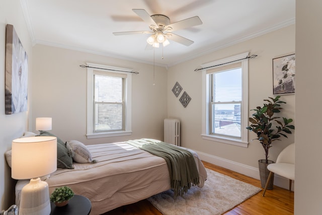 bedroom with ornamental molding, multiple windows, radiator heating unit, and wood finished floors