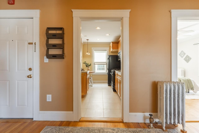 hall with baseboards, radiator heating unit, light wood-style flooring, and radiator