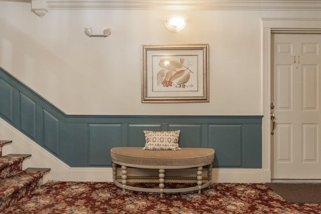 foyer featuring wainscoting, crown molding, stairway, and a decorative wall